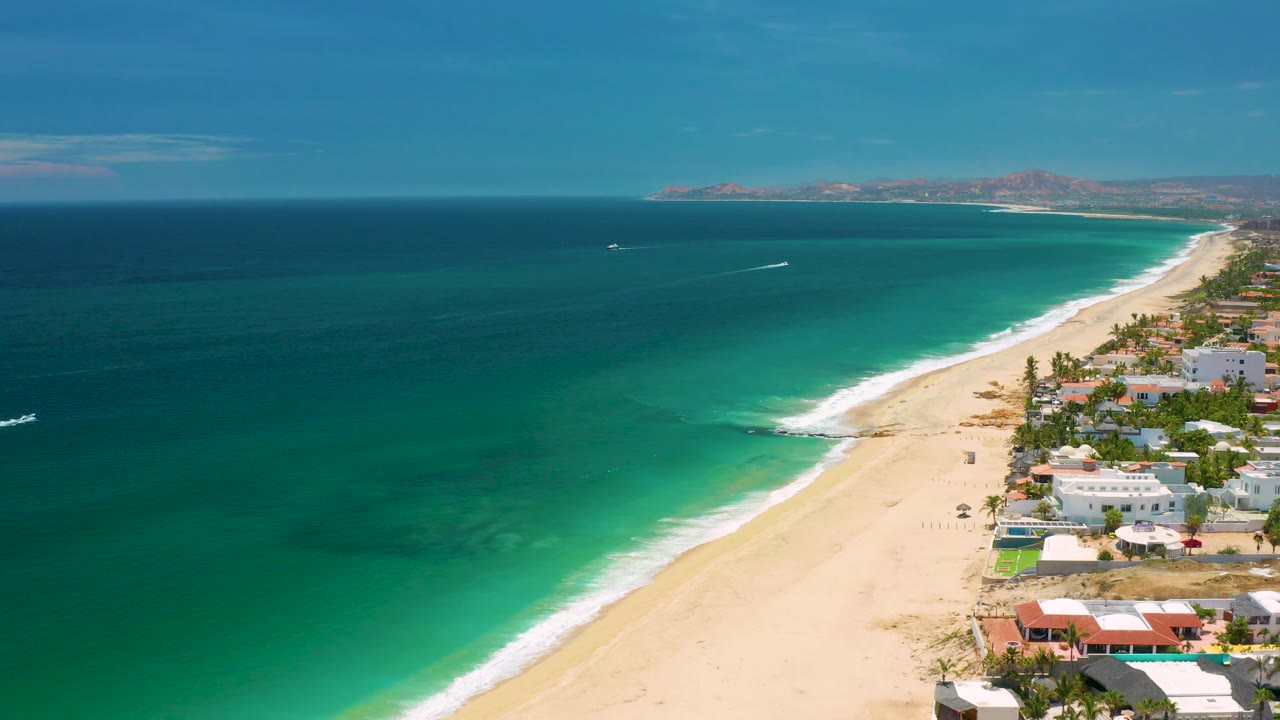 Third frame shows the San Jose del Cabo beach from above with darker ocean occupying more of the left side, white surf tracing the shore, buildings cropped along the right edge, distant land across the horizon, and no visible people.