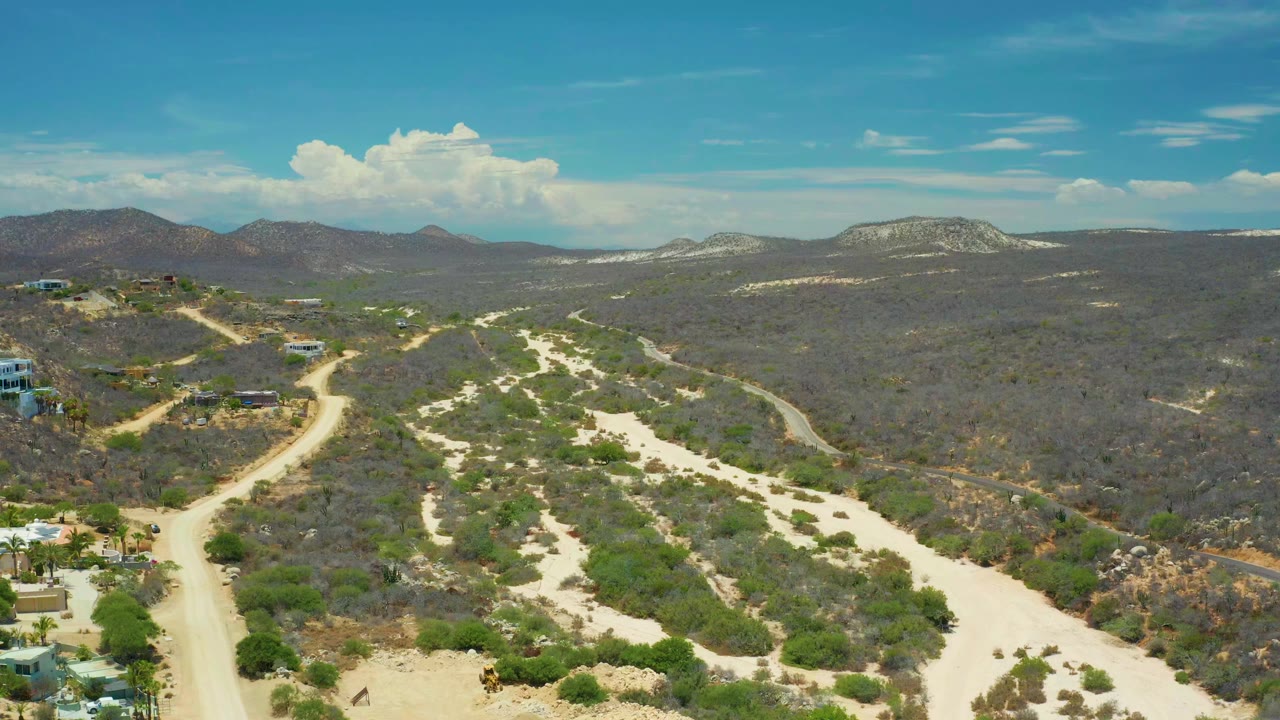 Aerial opening view in San Jose Del Cabo, Mexico, showing pale dirt roads cutting through dry scrub toward low mountains, with no visible people.