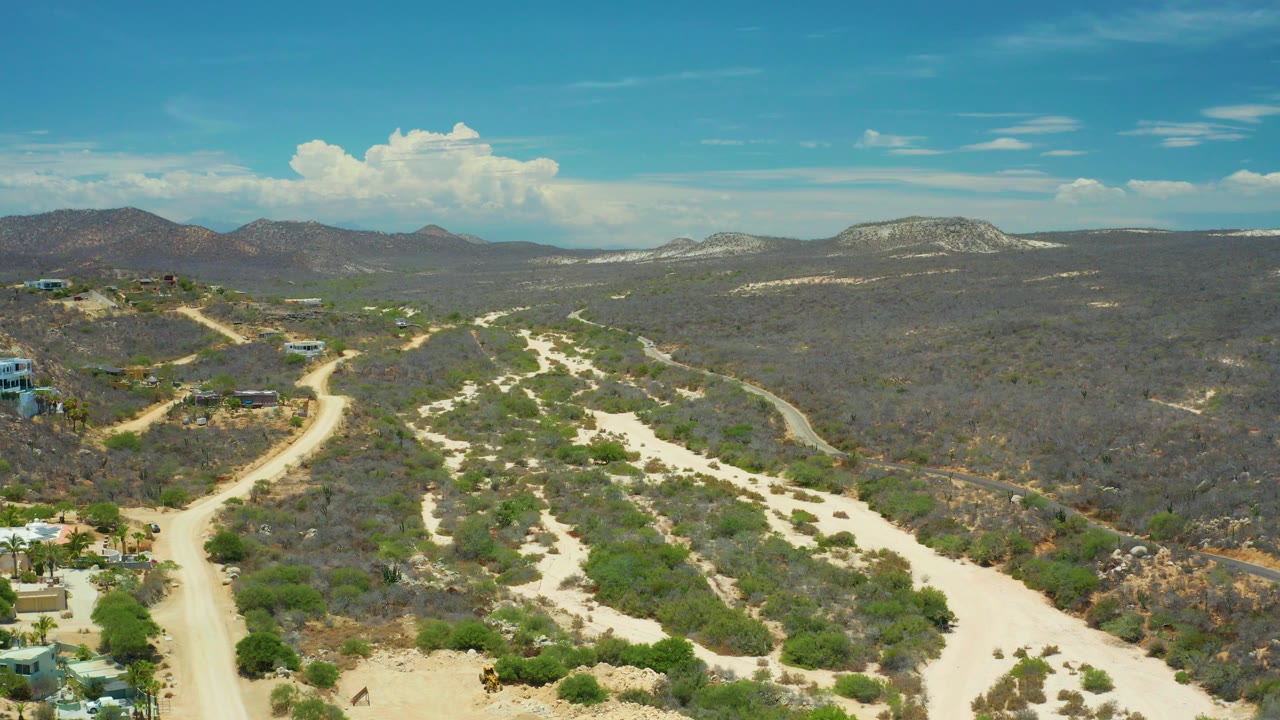 Aerial view of San Jose Del Cabo dry valley trails, sandy channels, dark green and brown brush, low mountains on the horizon, and no visible people.
