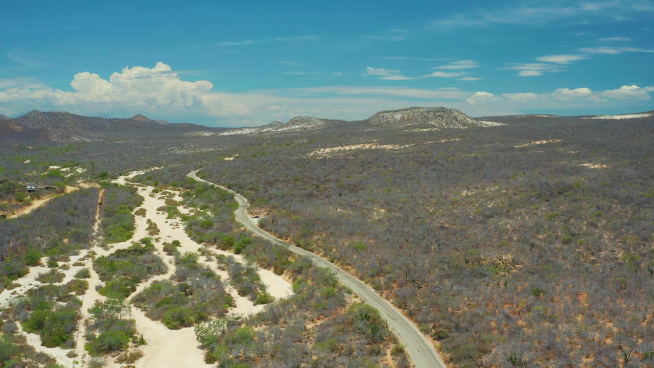 Aerial view of a winding road through dry scrubland and sandy paths.