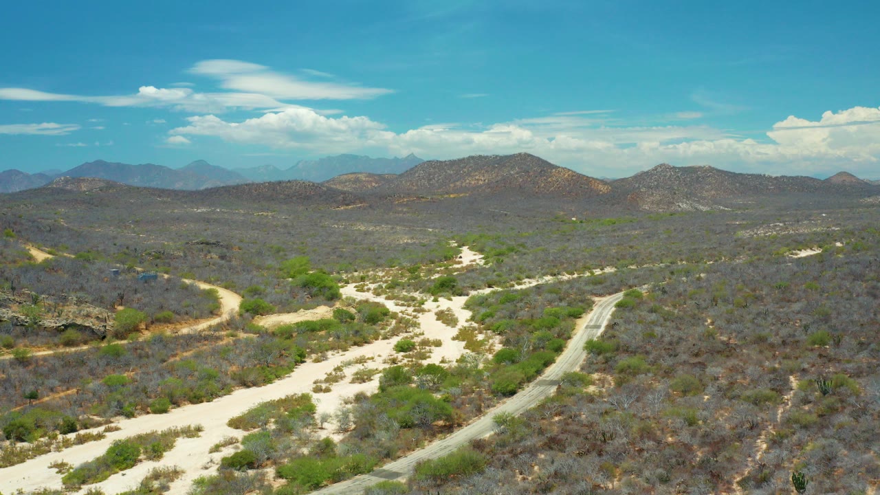 Aerial view of sandy wash, road, scrub hills, mountains, and blue sky.