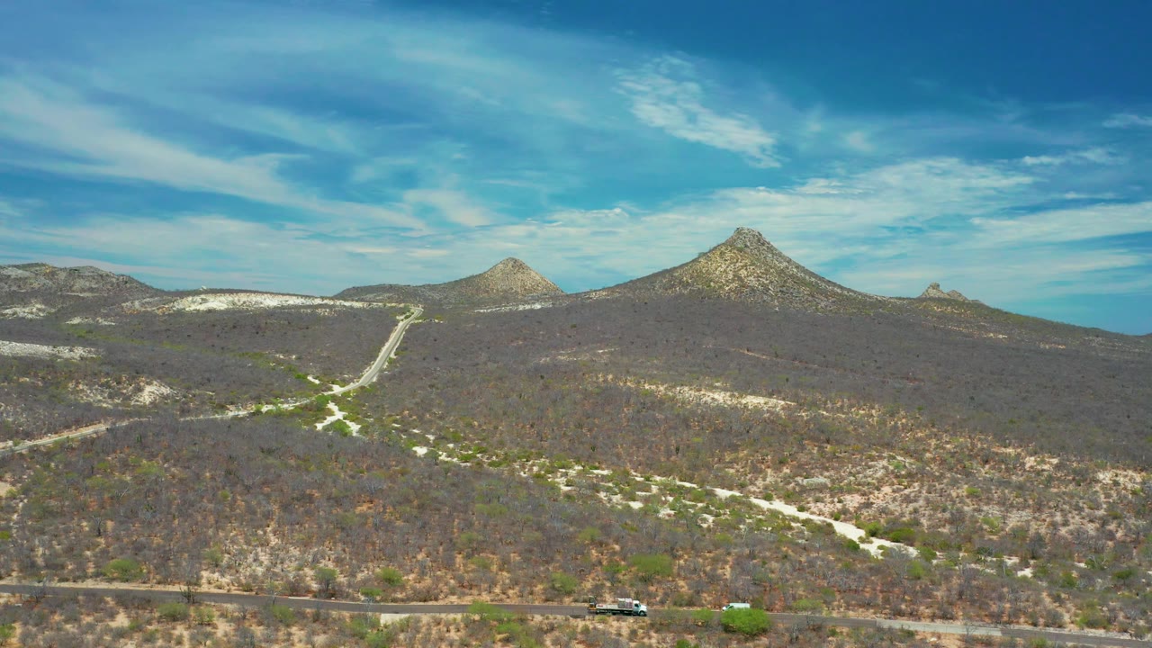 Scrub-covered hills and winding dirt paths below a blue sky with thin clouds.
