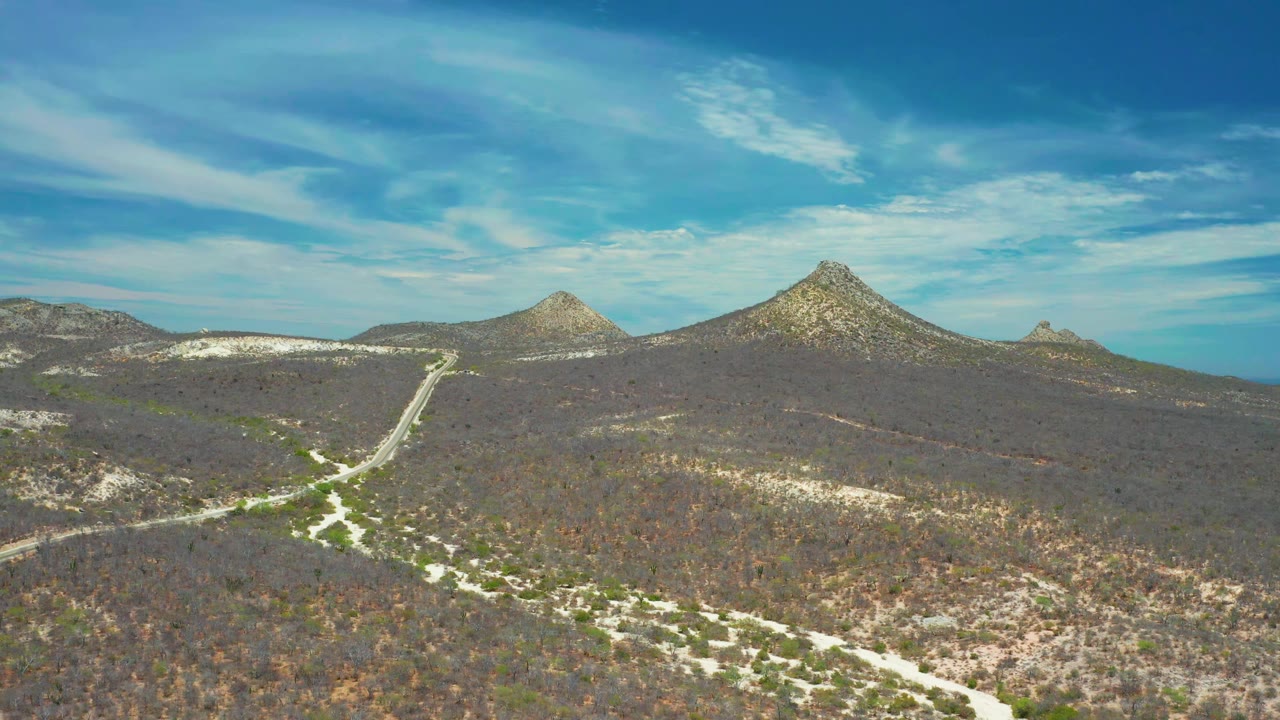 Aerial landscape with intersecting dirt roads, low brush, rocky hills, and clouds.