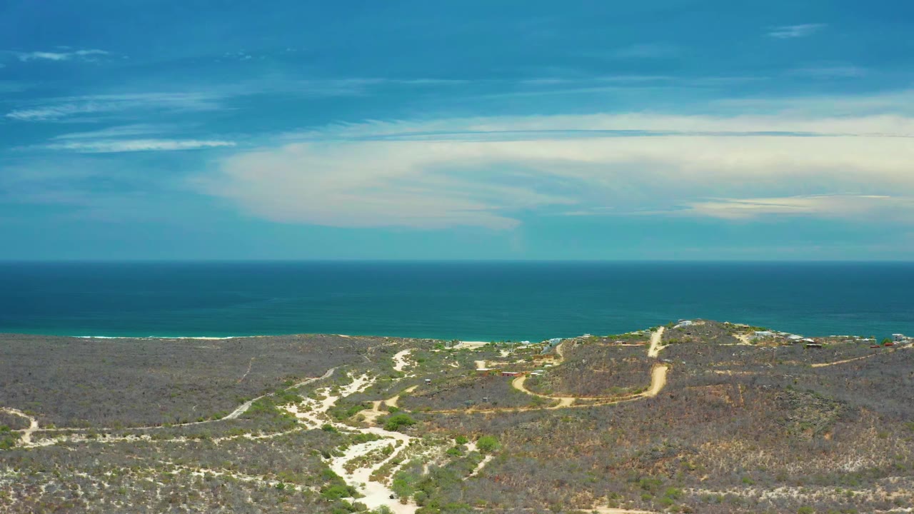 Aerial coastal landscape with sandy tracks, scrub, ocean band, and cloud-filled sky.