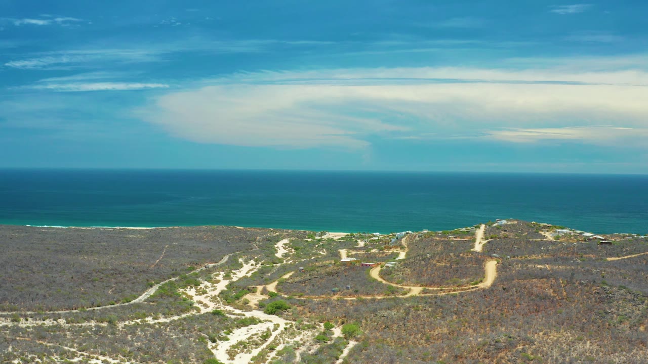 San Jose Del Cabo aerial view with scrub-covered land and light sand patches in the lower frame, blue water across the middle, and no visible people.