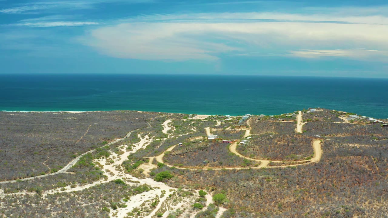 Aerial view in San Jose del Cabo showing the reserve from slightly farther along the coast, with branching sand paths, sparse green patches, distant surf, and no visible people.