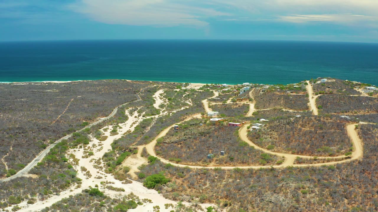 Aerial San Jose Del Cabo view with intersecting sandy paths across dry vegetation, a thin beach line, blue sea beyond, and no visible people.