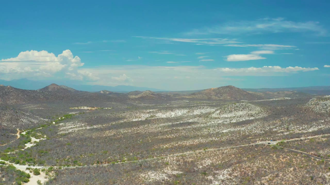 Scrub-covered desert basin with rounded hills and bright clouds