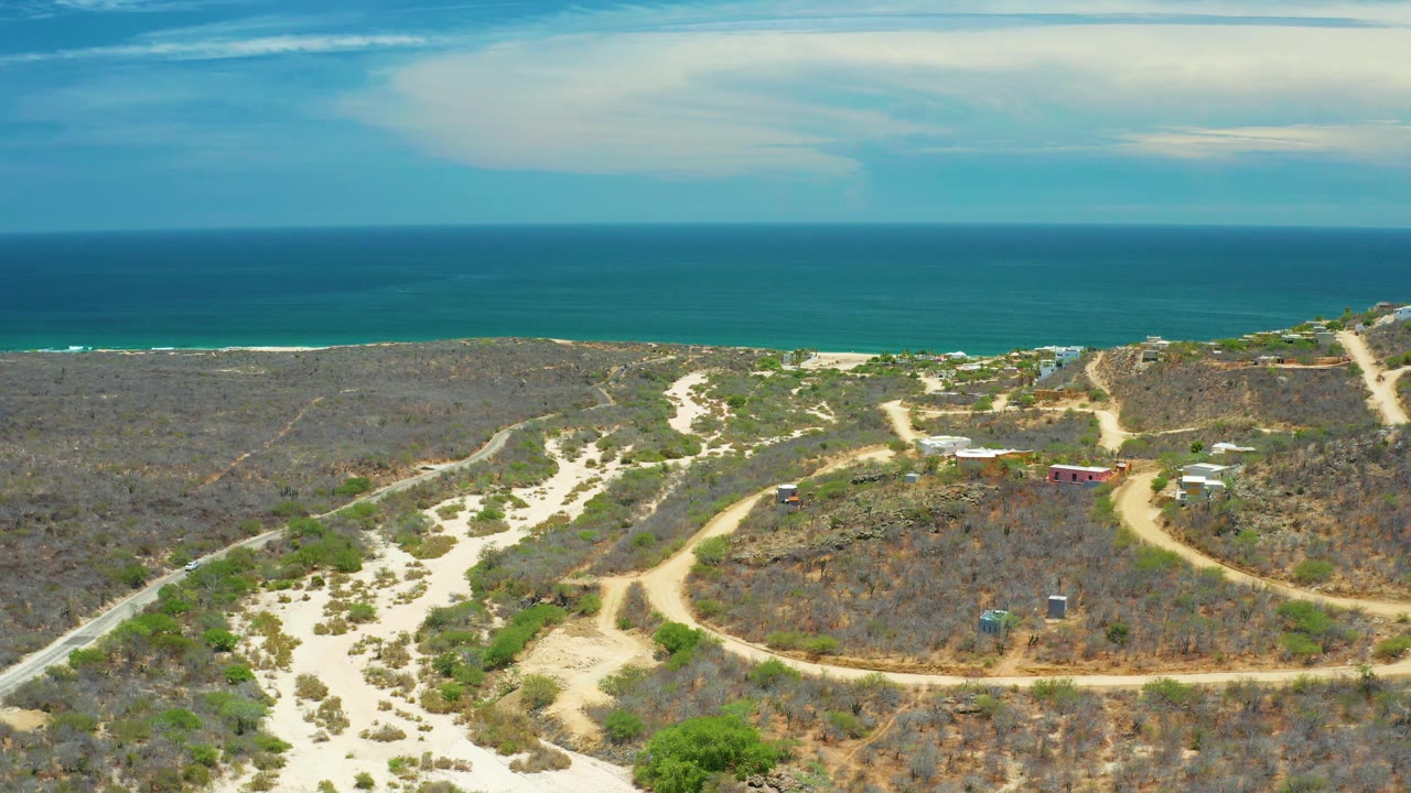 Remote coastal landscape with sandy wash, brush, and ocean horizon