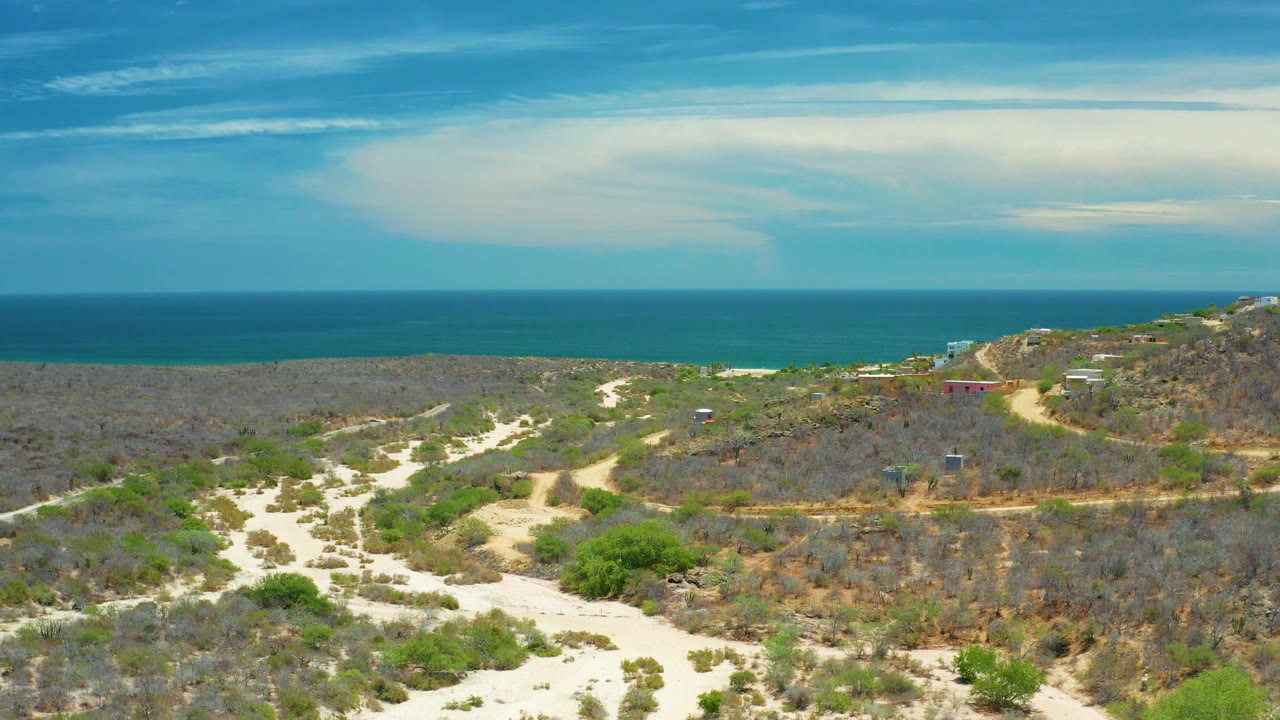 Open scrub landscape with pale roads, distant sea, and a wide cloud bank.