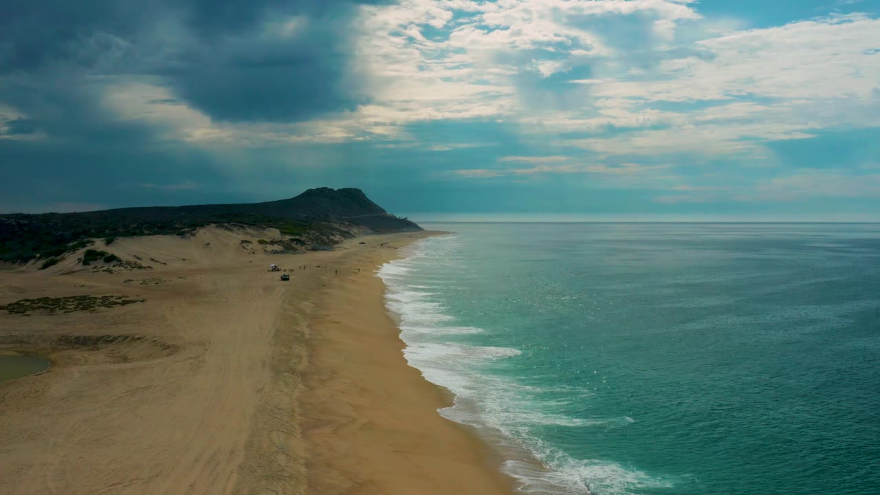 Laguna Beach, Baja California Sur appears from above with a broad empty sand strip, blue-green water, a white surf edge, a darker inland ridge, and no visible people.
