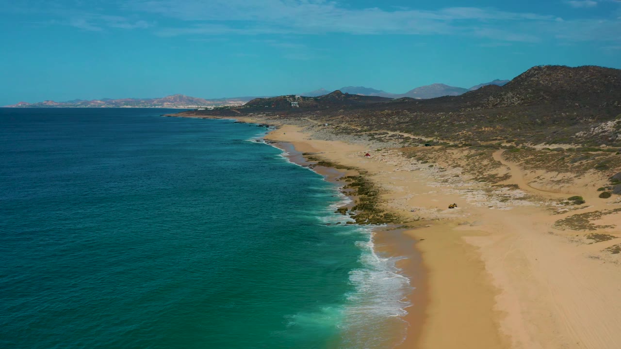 Laguna Beach, Baja California Sur appears from above with darker blue offshore water, lighter turquoise shallows, an empty sand strip, dunes, and no visible people.