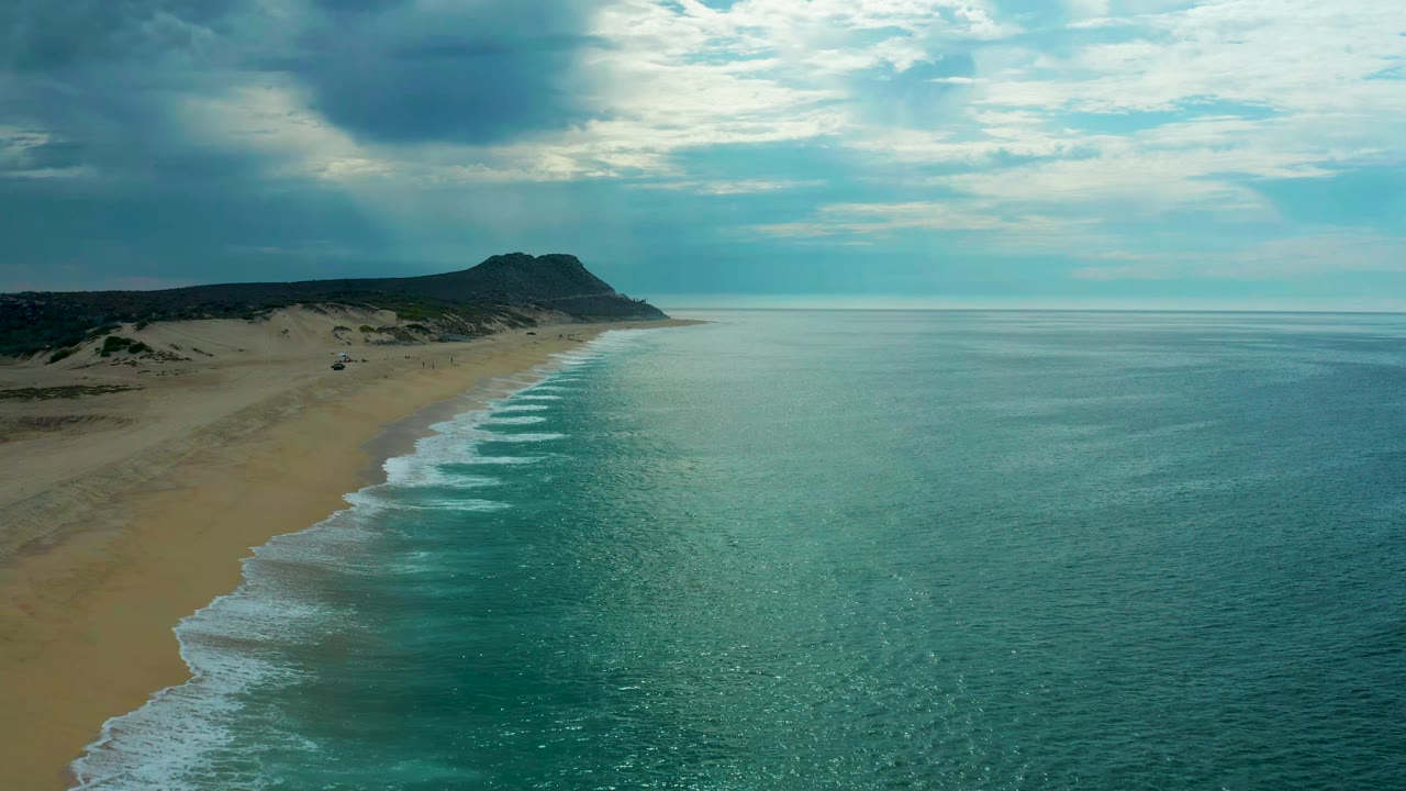 Wide drone-style view of Laguna Beach, Baja California Sur, showing repeated white wave bands along the sand and no visible people.