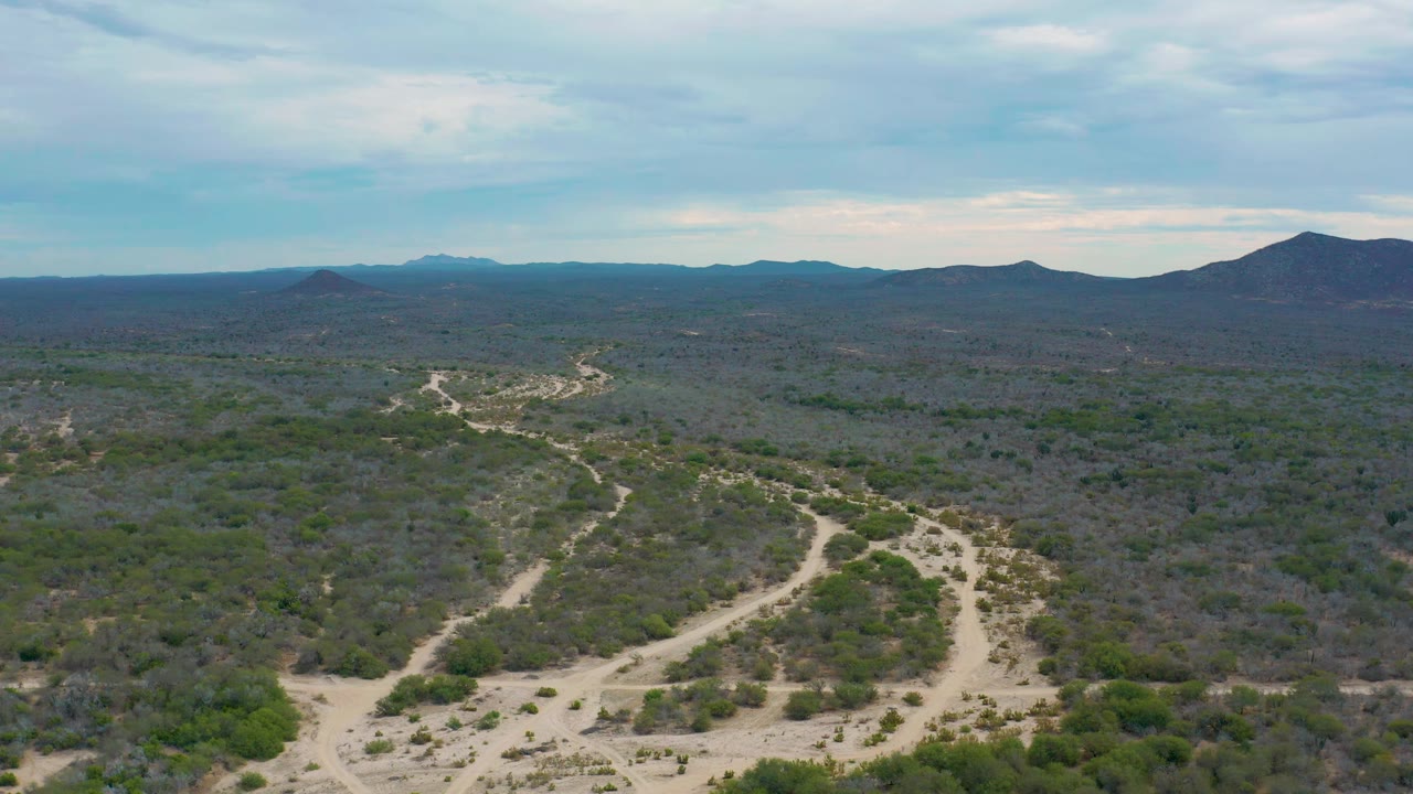 Aerial frame over Laguna Beach, Baja California Sur, showing branching sandy roads through scrubland, a broad cloudy sky, and no visible people.