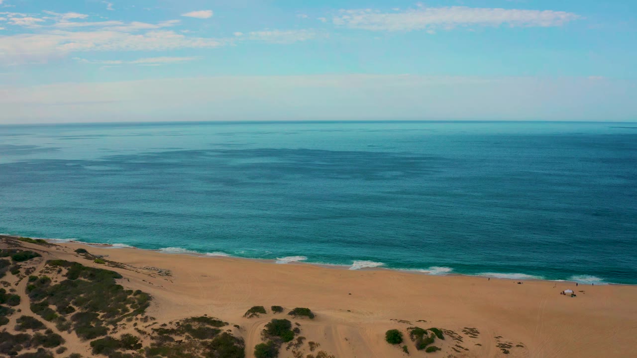 Laguna Beach coastline with the horizon stretching across the upper frame, turquoise shallows near the sand, darker blue water offshore, and no visible people.