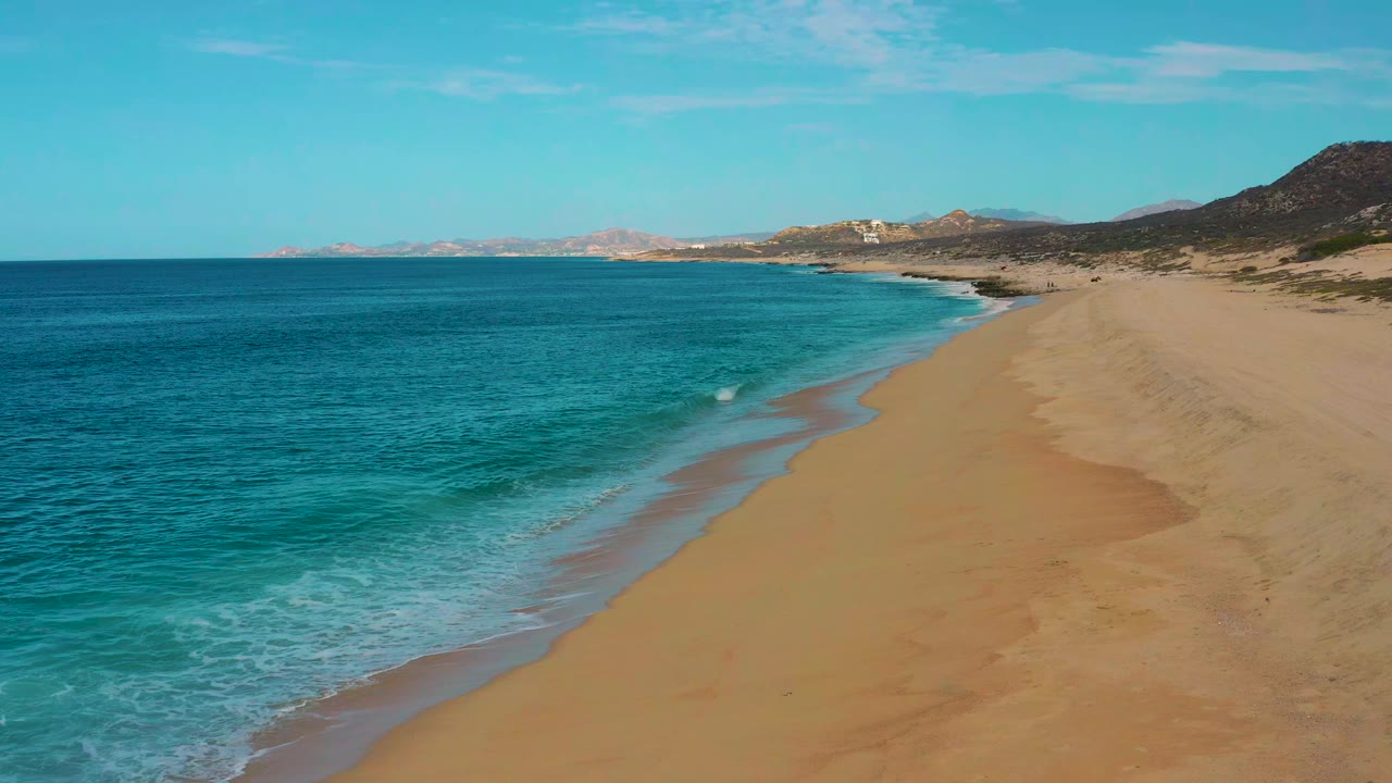 Aerial view over Laguna Beach, Baja California Sur, with small white waves reaching farther up the shoreline and no visible people on the sand.