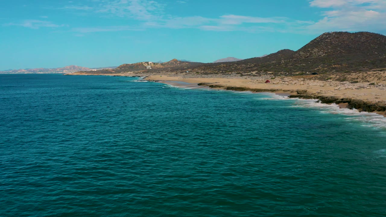 Laguna Beach, Baja California Sur aerial view with turquoise water taking most of the frame, pale sand to the right, scrub-covered hills behind it, and no visible people.