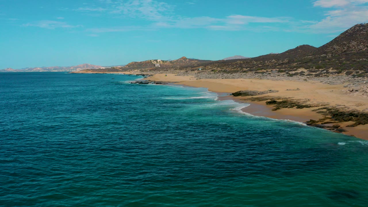 Aerial view of blue ocean beside a sandy beach and hills.