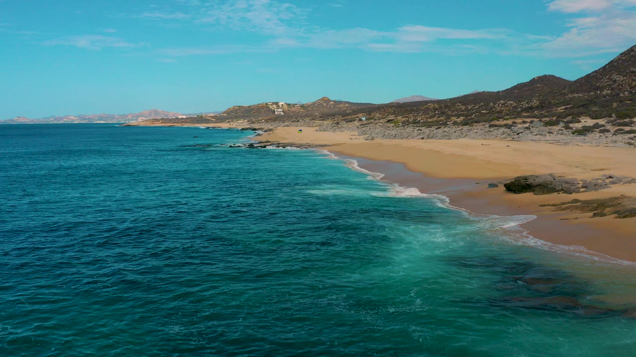 Aerial coastline with turquoise ocean, sandy beach, and rocky hills