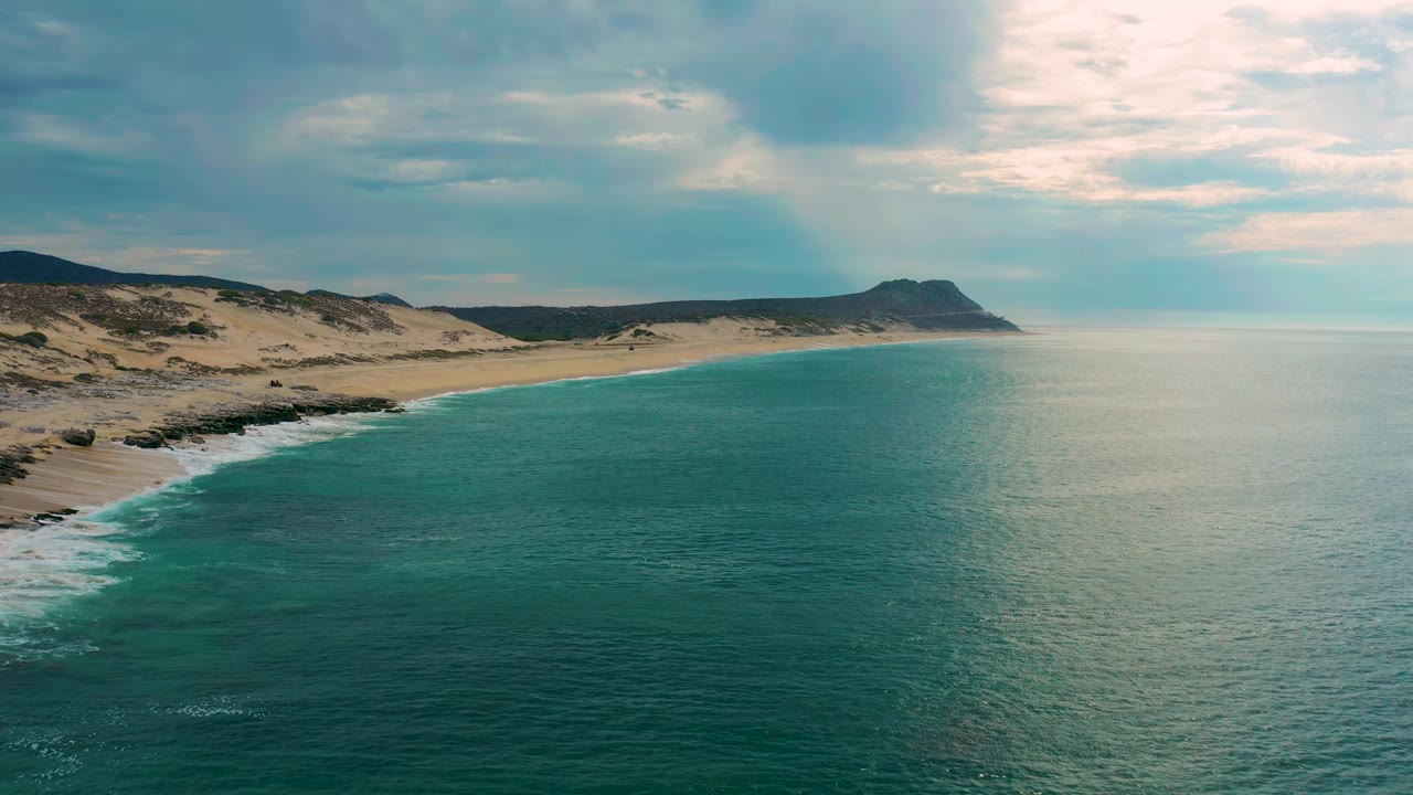 Aerial frame over Laguna Beach, Baja California Sur, showing the shoreline slightly farther along the frame, with small white surf lines on the left and no visible people.