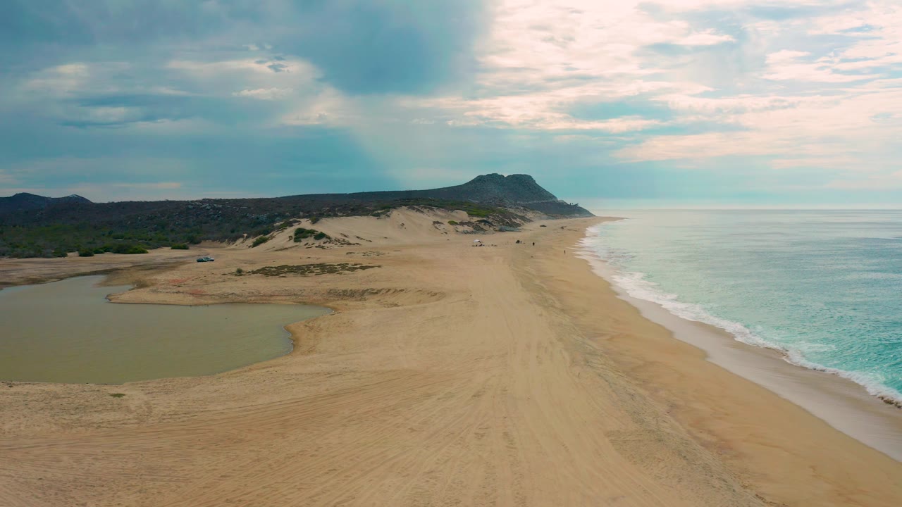 Laguna Beach, Baja California Sur appears from above with a curved lagoon in the foreground, sandy flats through the center, ocean surf to the right, darker cloud over land, and no visible people.