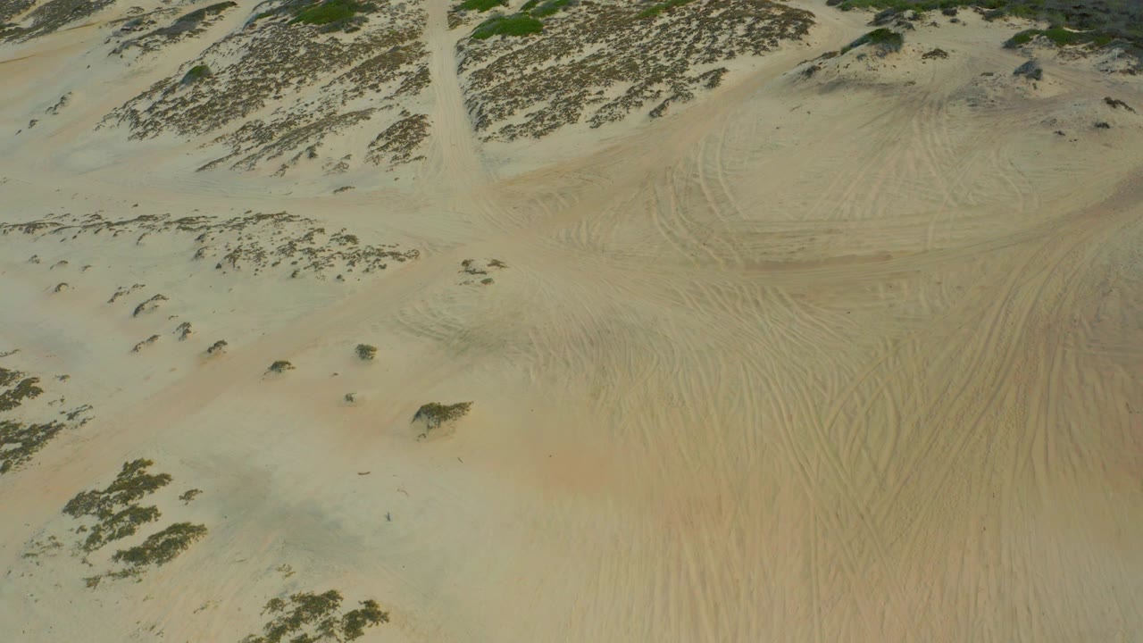 Oblique aerial frame from Laguna Beach, Baja California Sur showing sand ripples, scrub clusters across the upper slope, visible track lines, and no visible people.