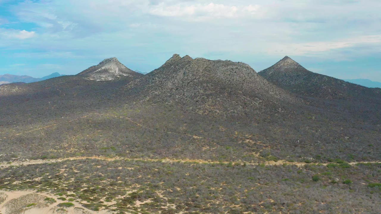 Wide aerial view of rocky mountains and sandy scrubland in Laguna Beach, Baja California Sur, Mexico, with blue sky overhead and no visible people.