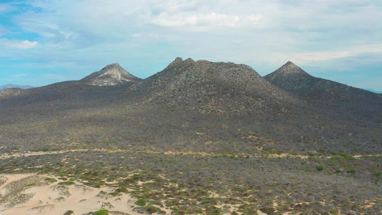 Low aerial mountain view with sandy tracks, scrub vegetation, and layered clouds.