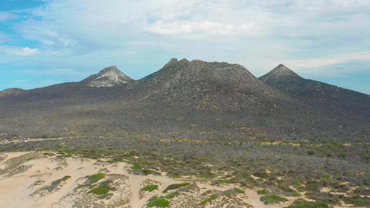 Aerial view of rocky mountains rising behind scrubland and pale dune tracks.
