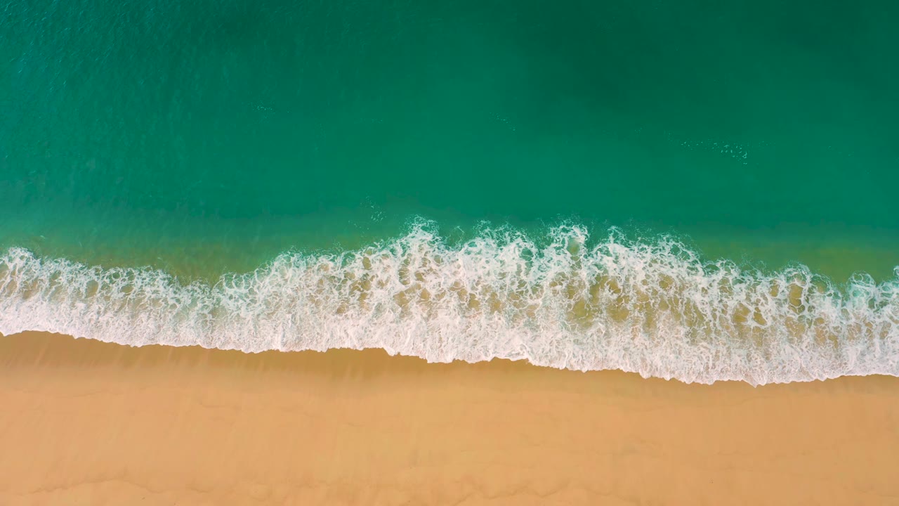 A wider band of white foam spreads along the shore beneath green-blue ocean water at Laguna Beach, Baja California Sur, with no visible people.