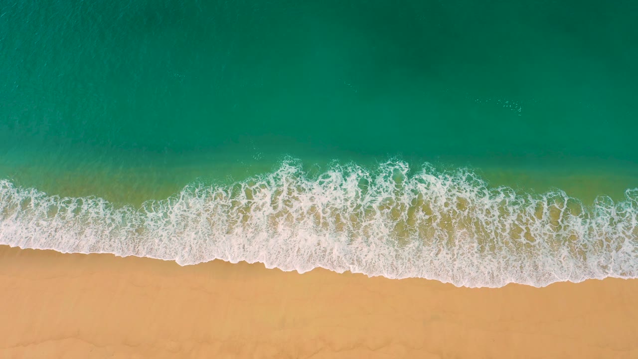White surf curls across a clean sandy beach under turquoise water at Laguna Beach, Baja California Sur, with no visible people or structures.