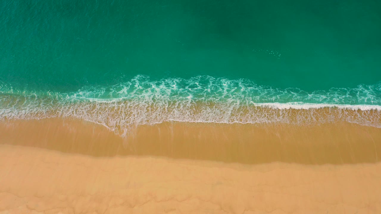 Overhead view of turquoise water meeting tan sand at Laguna Beach in Baja California Sur, with a thin white foam line and no visible people.