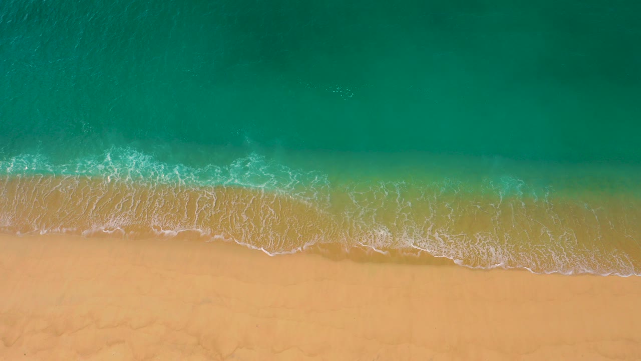 Overhead frame from Laguna Beach, Baja California Sur, showing turquoise water meeting pale sand with a thin white foam edge and no visible people.