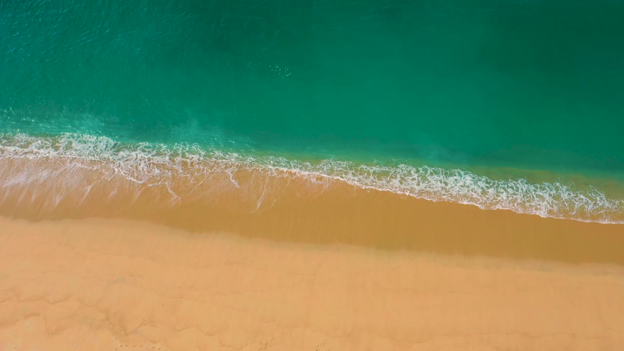Top-down view of a curving white surf line over golden yellow sand, with emerald water above it at Laguna Beach, Baja California Sur, and no visible people.