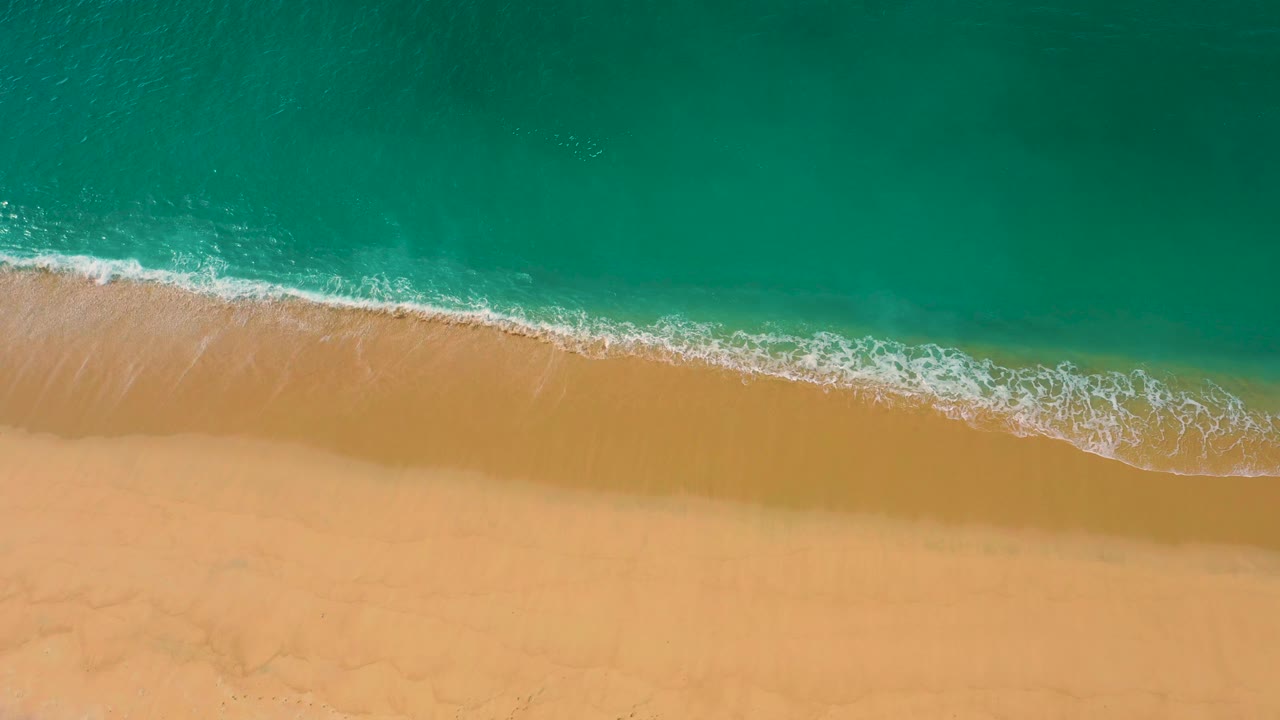 Aerial shoreline frame where the foam line runs diagonally between emerald water and yellow sand at Laguna Beach, Baja California Sur, with no visible people.