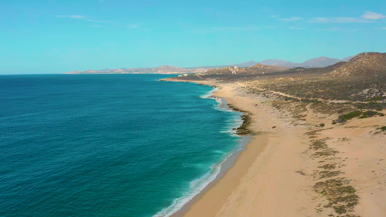 High coastal view with blue-green water, empty sand, and desert hills.