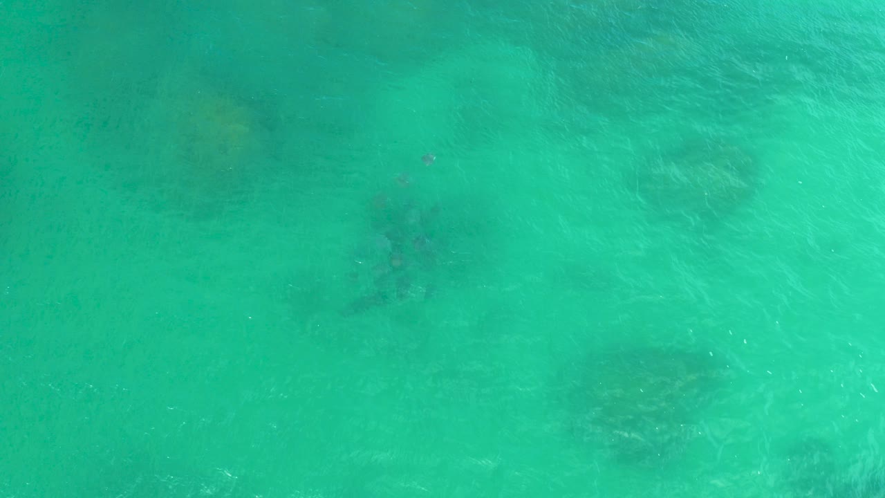 Overhead view of turquoise sea water in Laguna Beach, Baja California Sur, with faint darker submerged rock patches and no visible people.