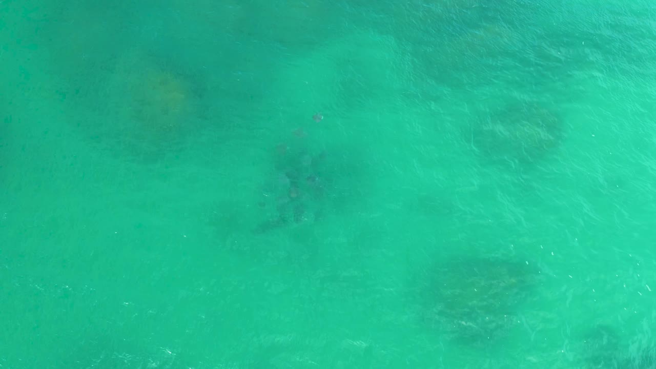 Clear green-blue water with soft surface ripples and darker seabed shapes.