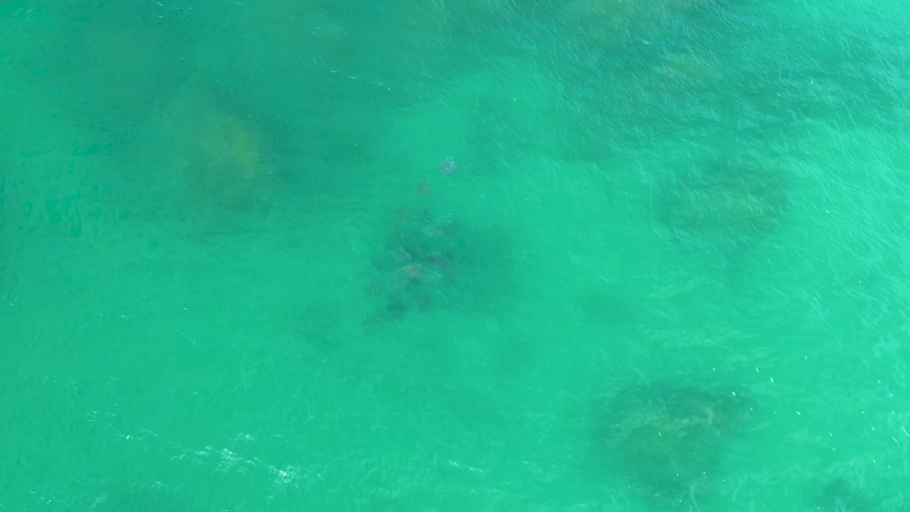 Turquoise ocean surface in Laguna Beach, Baja California Sur, shows small dark submerged rock areas beneath moving light and no visible people.
