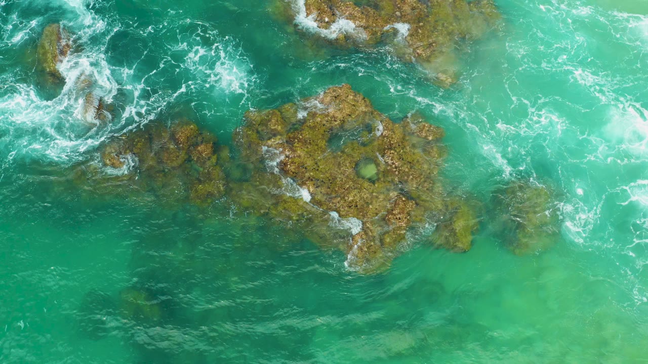 Overhead view of green ocean water washing around brown rocks at Laguna Beach, Baja California Sur, with no visible people.