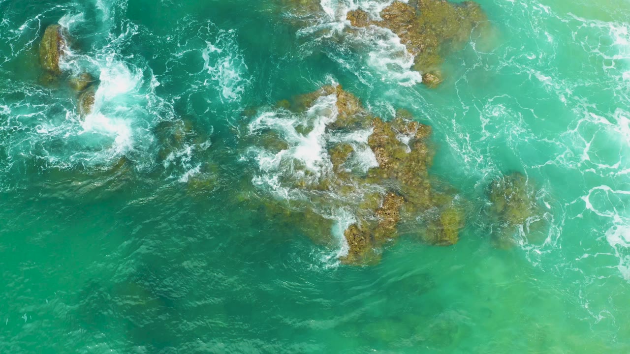 Clear green water reveals submerged rocks while white foam crosses the upper edge at Laguna Beach, Baja California Sur, with no visible people.