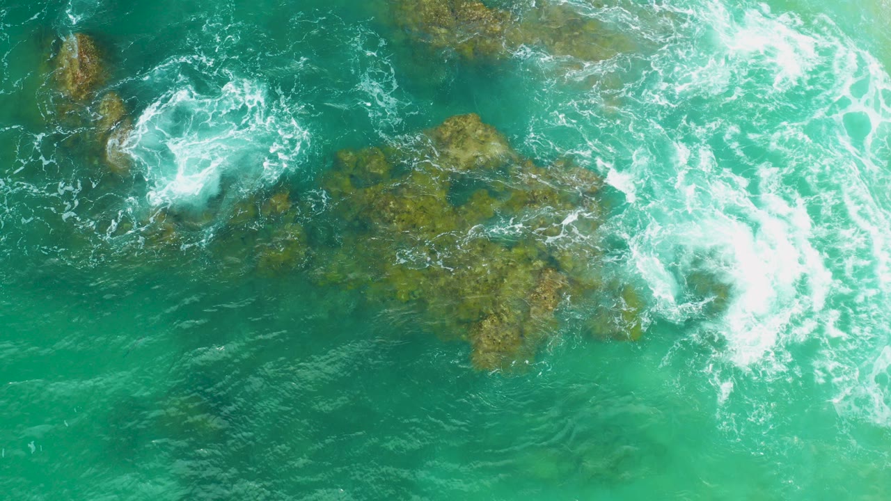 Turquoise surf breaking over coral rock from above