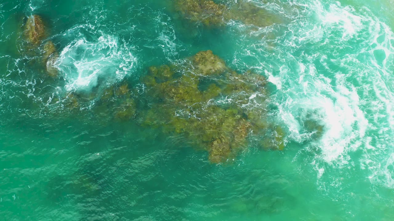 Overhead Laguna Beach frame with whitewater curling across the upper left and right of a brown-green coral formation, no visible people.