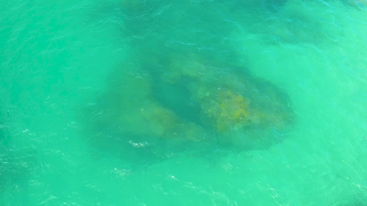 Blue-green water ripples over a central underwater rock mass in Laguna Beach, Baja California Sur, with no visible people.