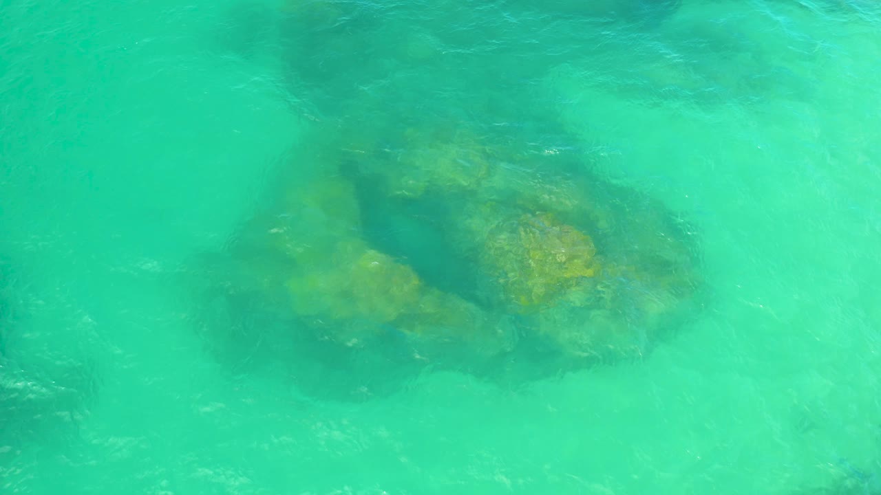 Overhead turquoise water surrounds a darker rock cluster that sits slightly lower in the frame in Laguna Beach, Baja California Sur, with no visible people.