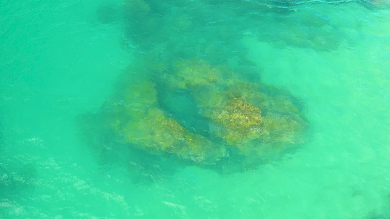Aerial view of turquoise water over dark submerged rocks in Laguna Beach, Baja California Sur, with no visible people.