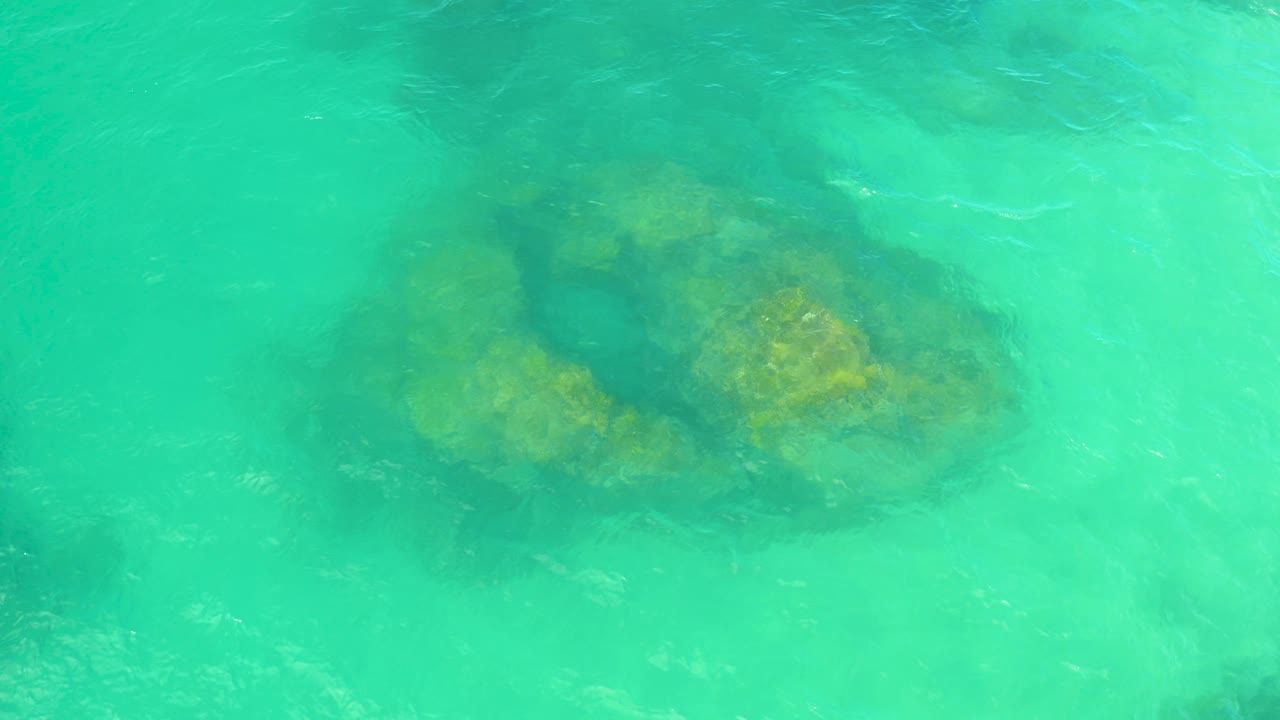 A mossy underwater boulder fills the lower-left area beneath turquoise ripples in Laguna Beach, Baja California Sur, with no visible people.