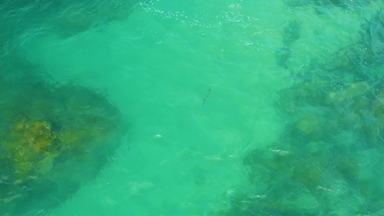 Clear green-blue sea water covers a darker central rock patch near Laguna Beach, Baja California Sur, with fine white highlights from small ripples and no visible people.