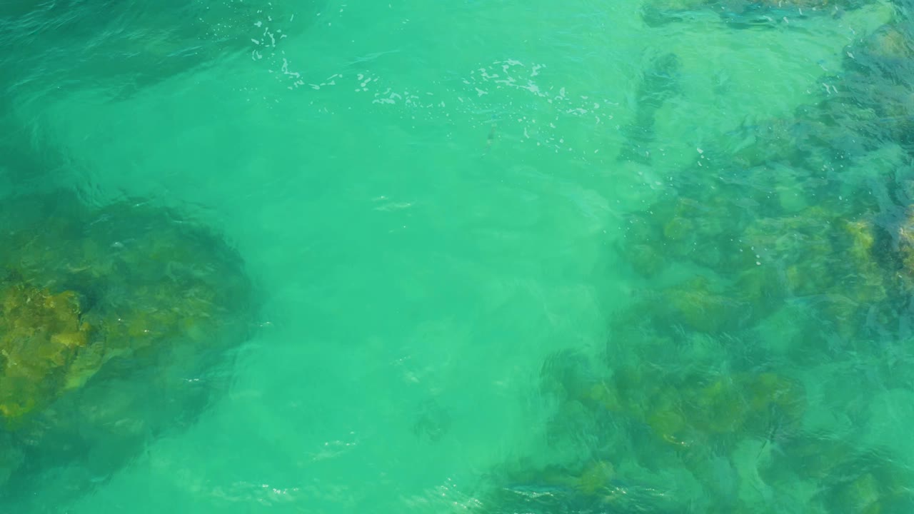 Clear shallow water in Laguna Beach, Baja California Sur, passes over dark underwater rocks near the center of frame, with no visible people.