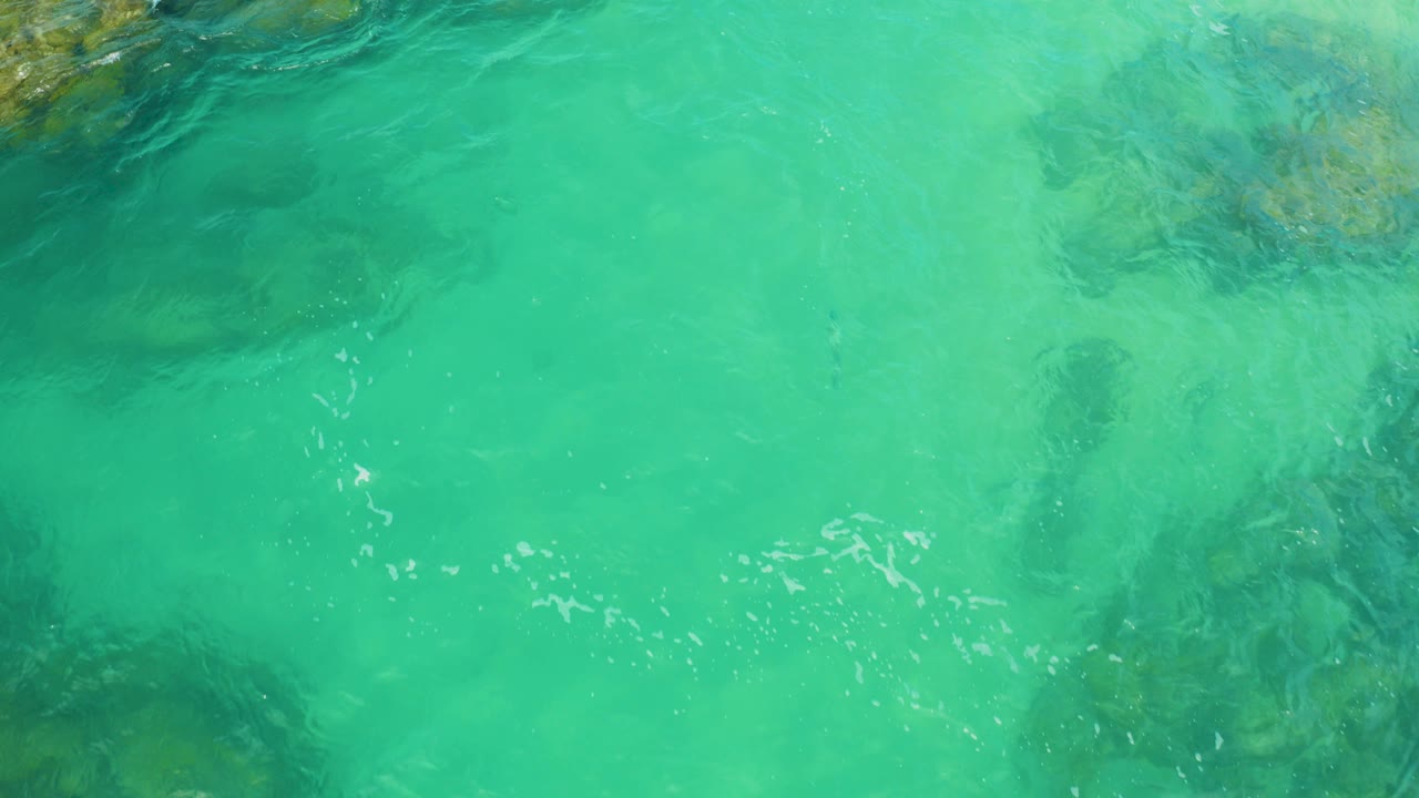 Top-down view of turquoise seawater and darker submerged rocks at Laguna Beach, Baja California Sur, with no visible people.